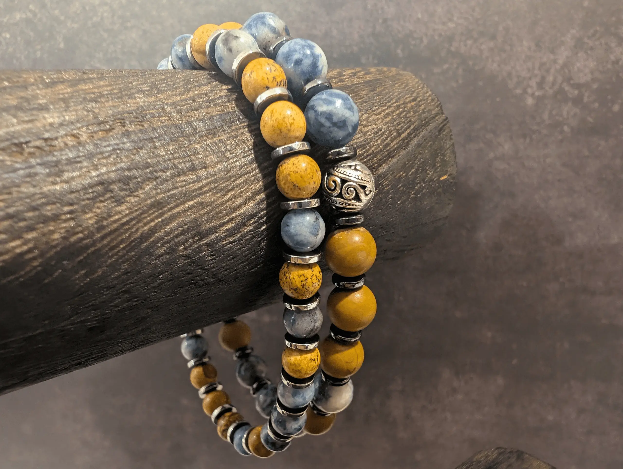 Two beaded bracelets with alternating yellow and blue stone beads separated by silver spacer rings, draped on a dark wooden log.