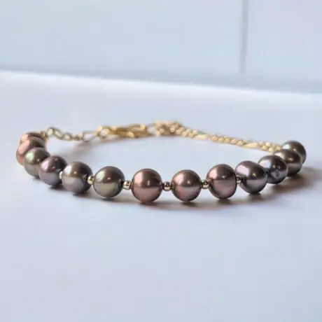 Brown pearl beaded bracelet with gold-tone chain clasp on white surface.