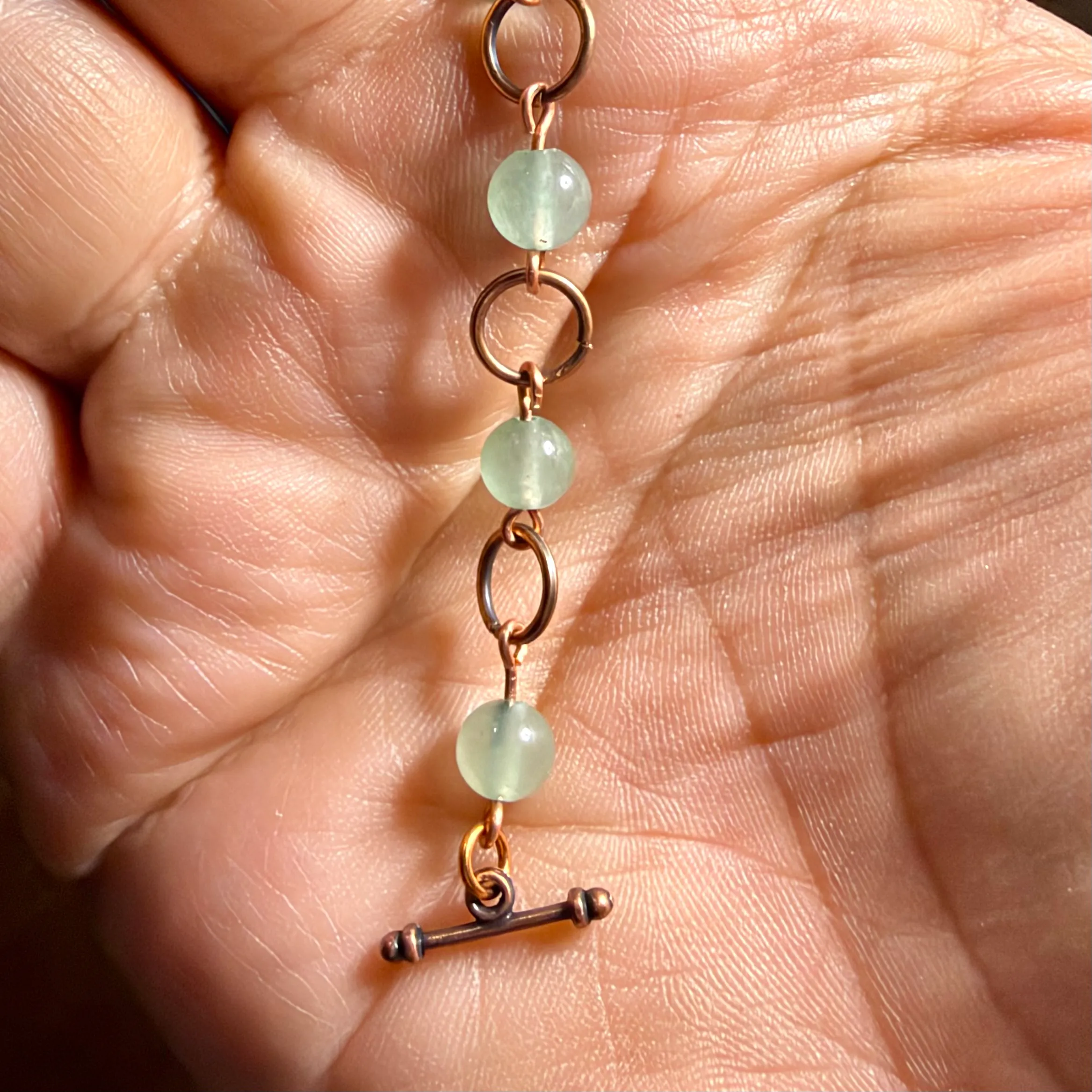 Copper bracelet with pale green gemstone beads and toggle clasp, held in hand.
