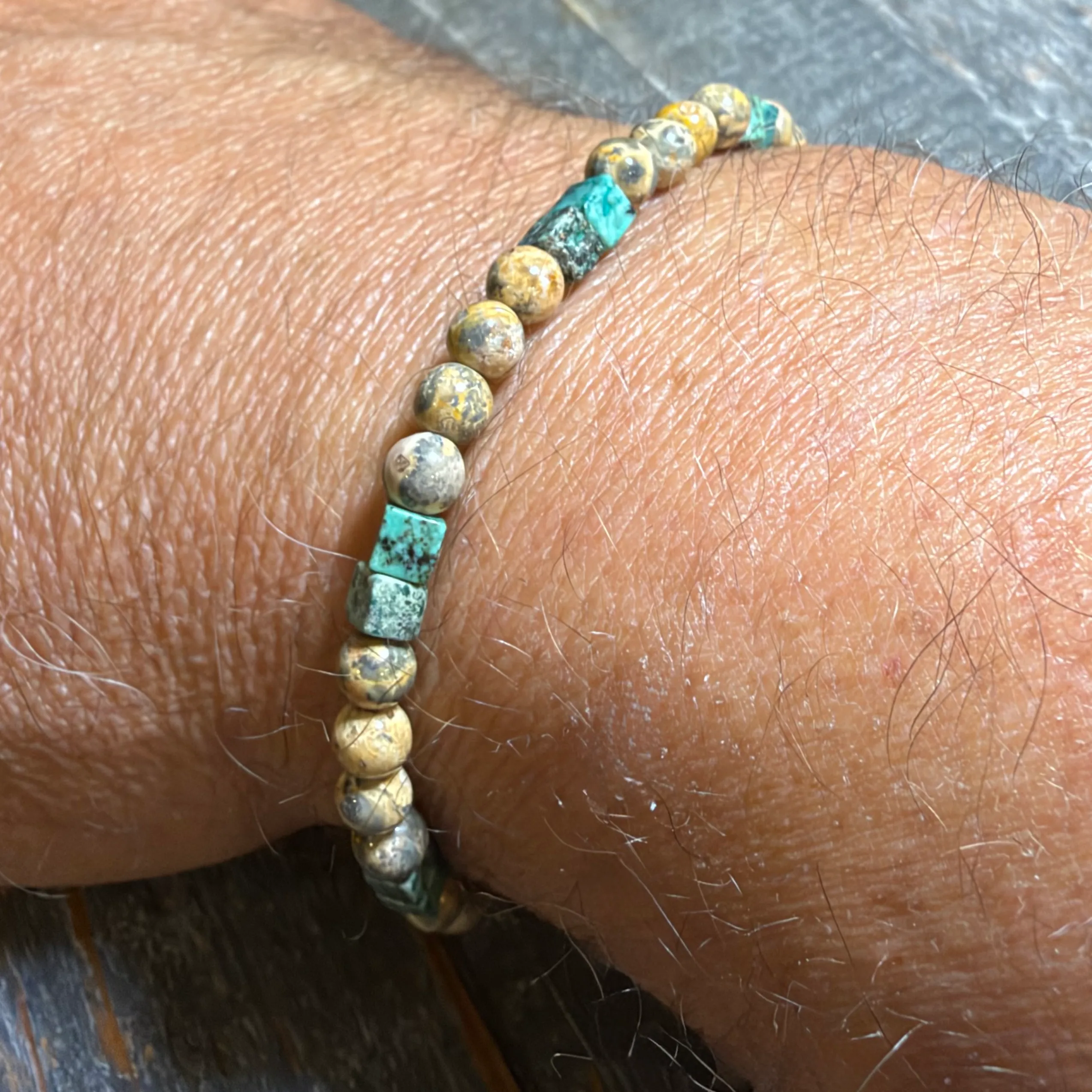 Beaded bracelet with turquoise and bronze metallic spherical beads on elastic cord worn on wrist.
