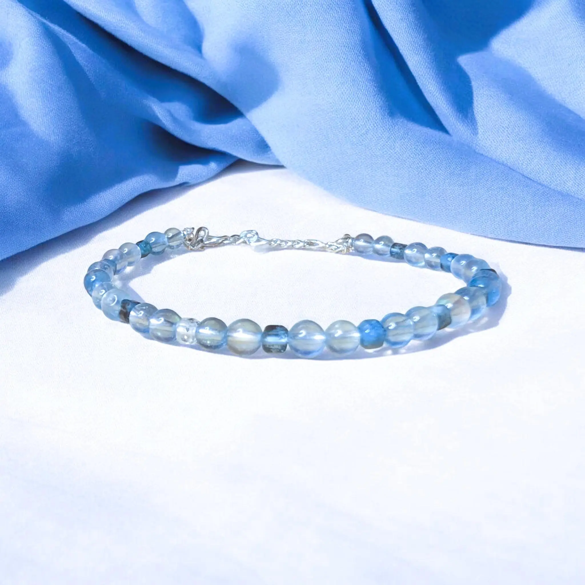 Clear blue faceted aquamarine beaded bracelet with silver chain clasp on white background.