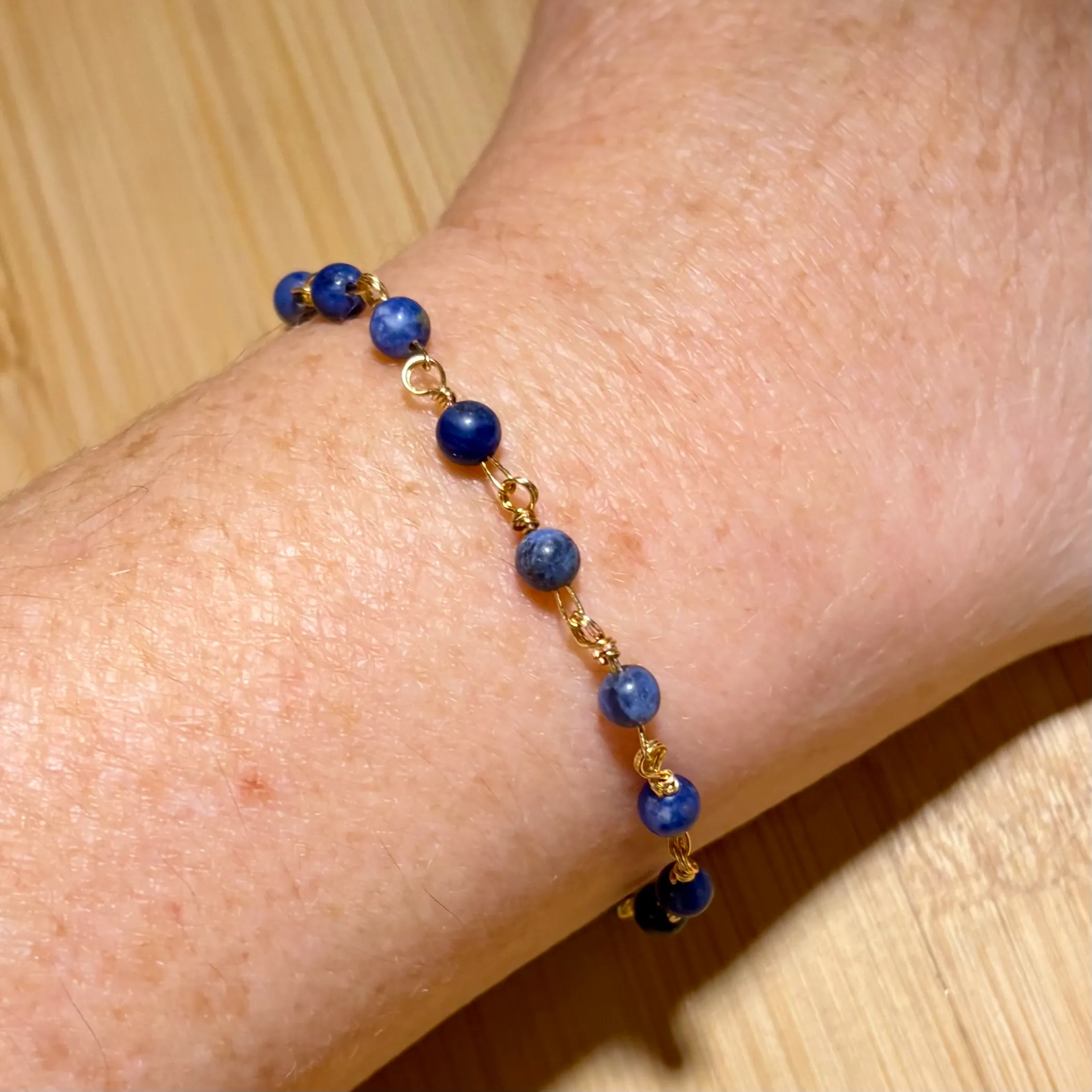 Blue lapis lazuli beaded bracelet with gold-tone wire links worn on a wrist.