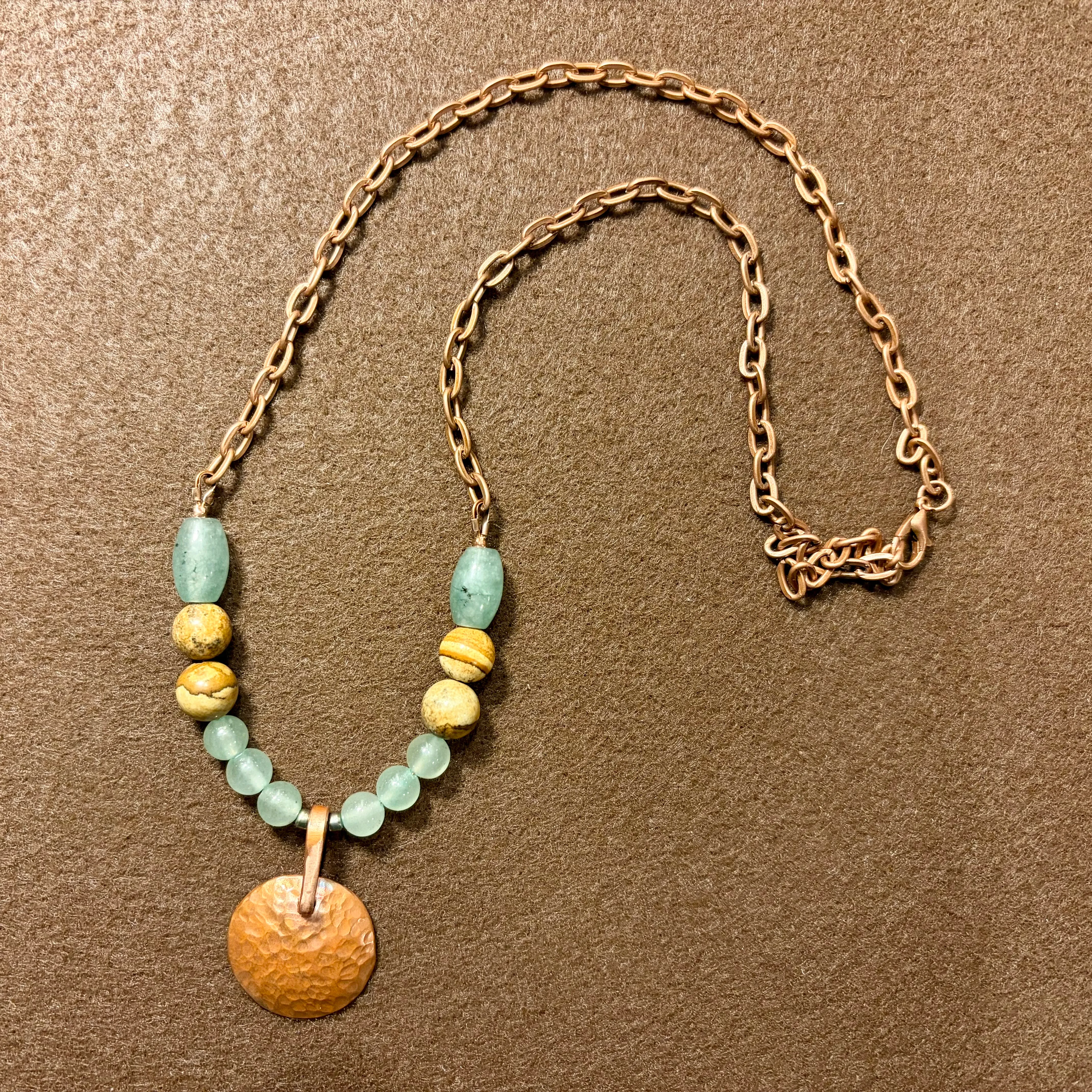 Gold chain necklace with pale green jade beads, textured gold spacer beads, and a hammered copper disc pendant.