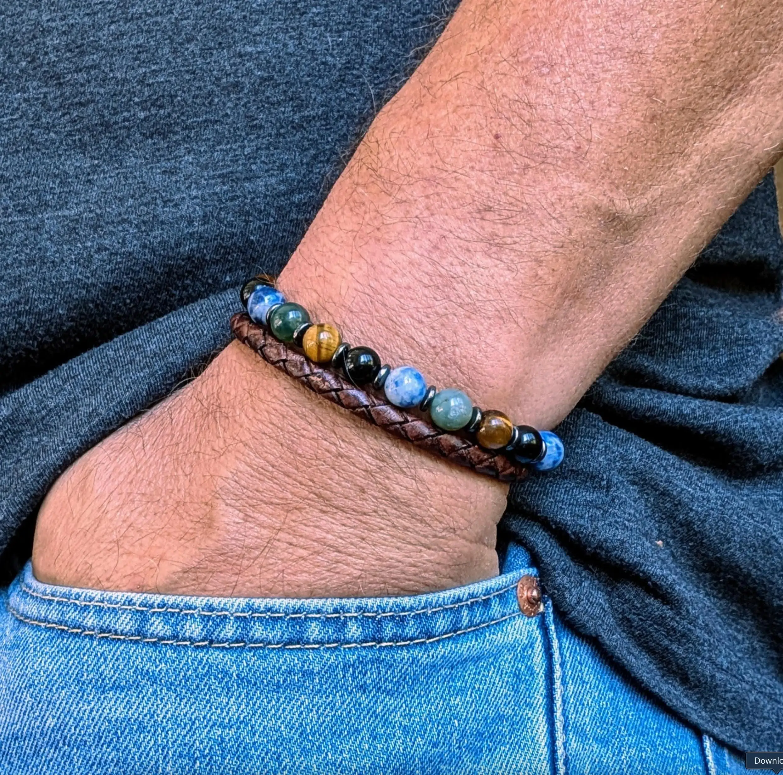 Man wearing brown leather bracelet with blue, green, black, and gold beads on wrist.