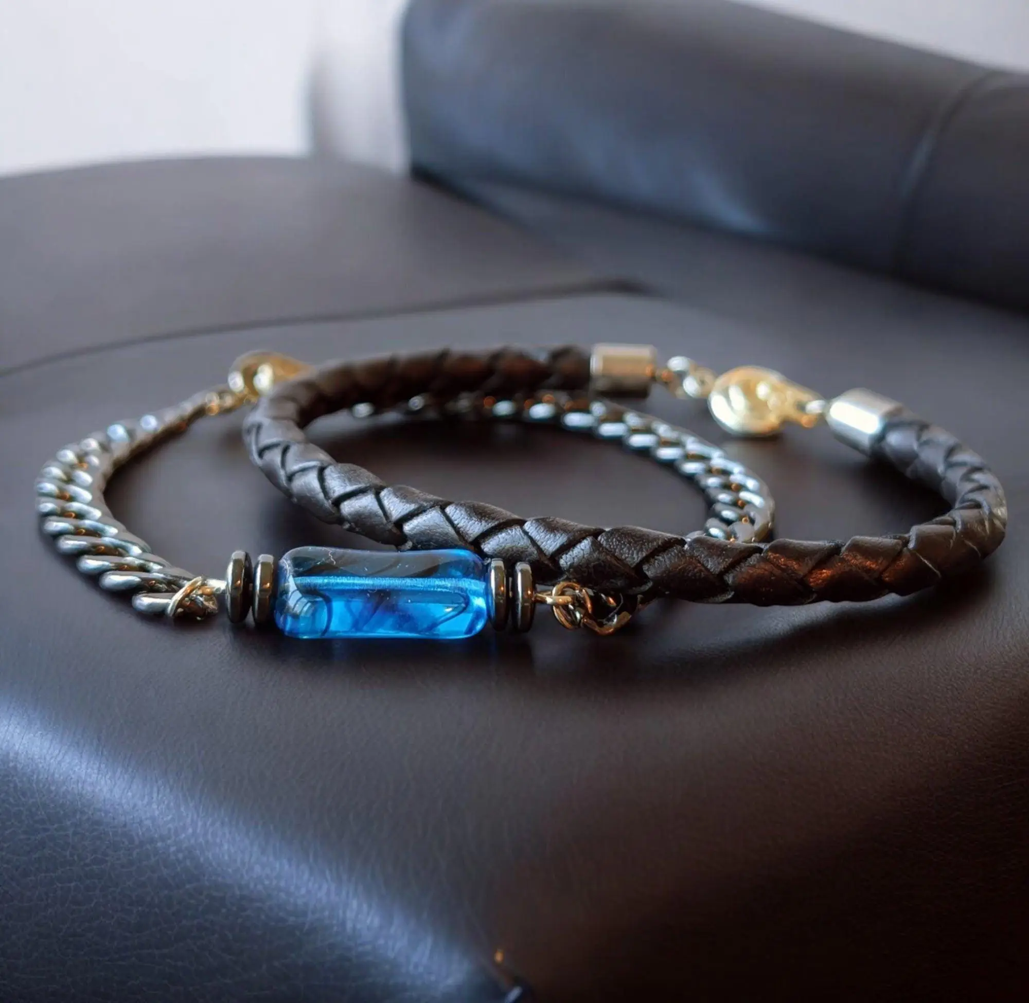 Brown leather braided bracelet with blue crystal centerpiece and gold-tone metal accents on dark surface.