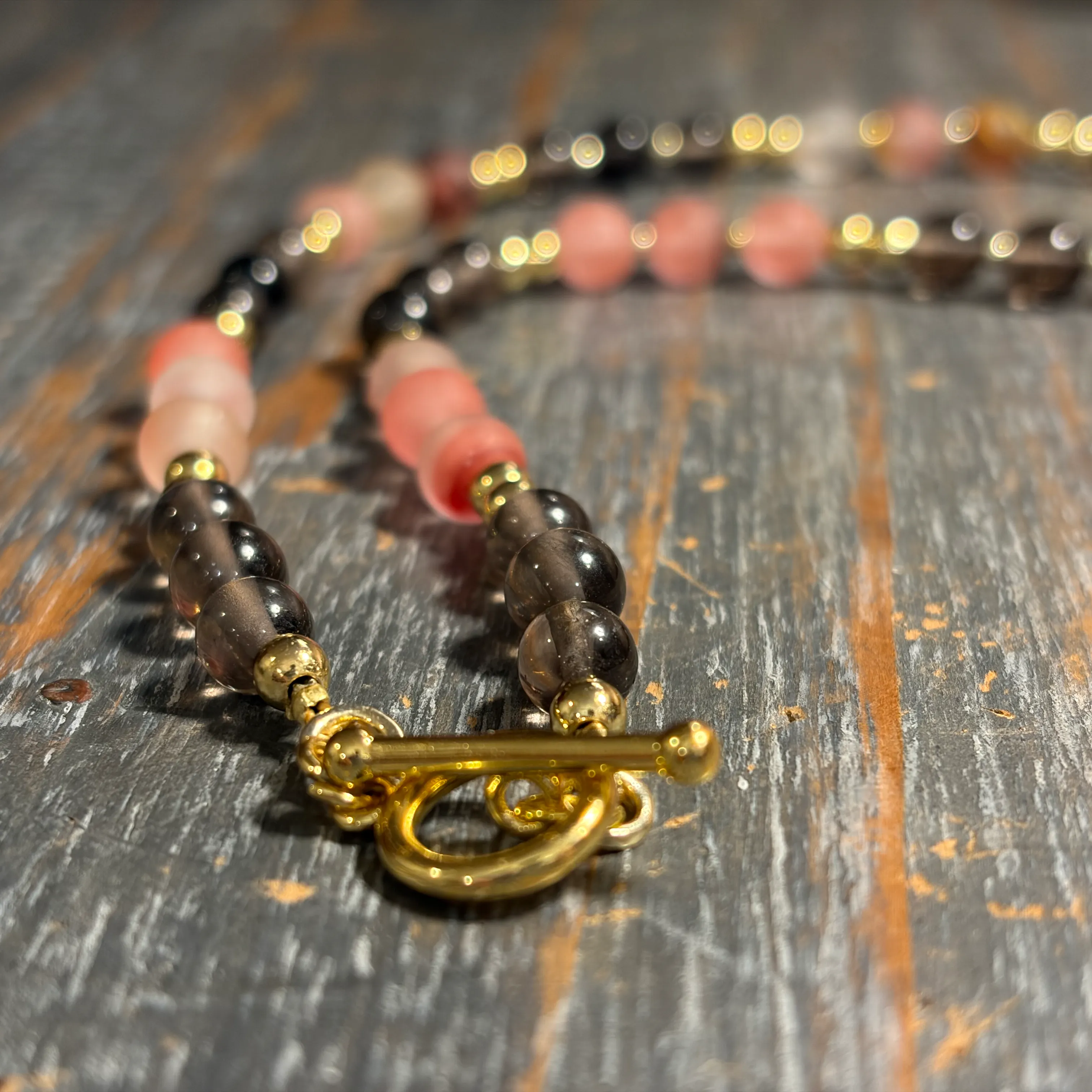 Beaded bracelet with black and coral beads, gold spacers, and ornate brass toggle clasp on wooden surface.