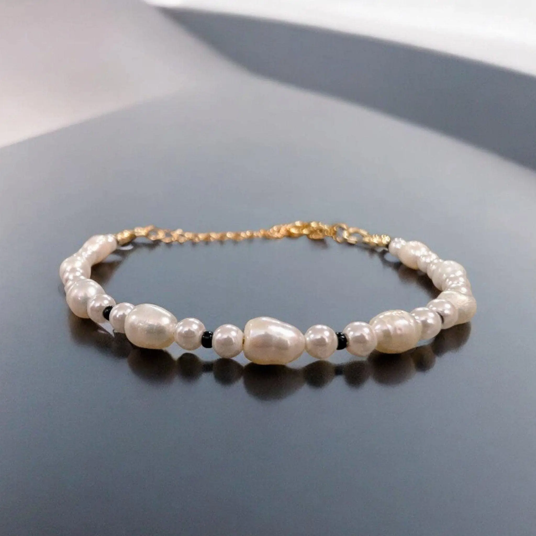 Pearl and black bead bracelet with gold-tone chain closure.