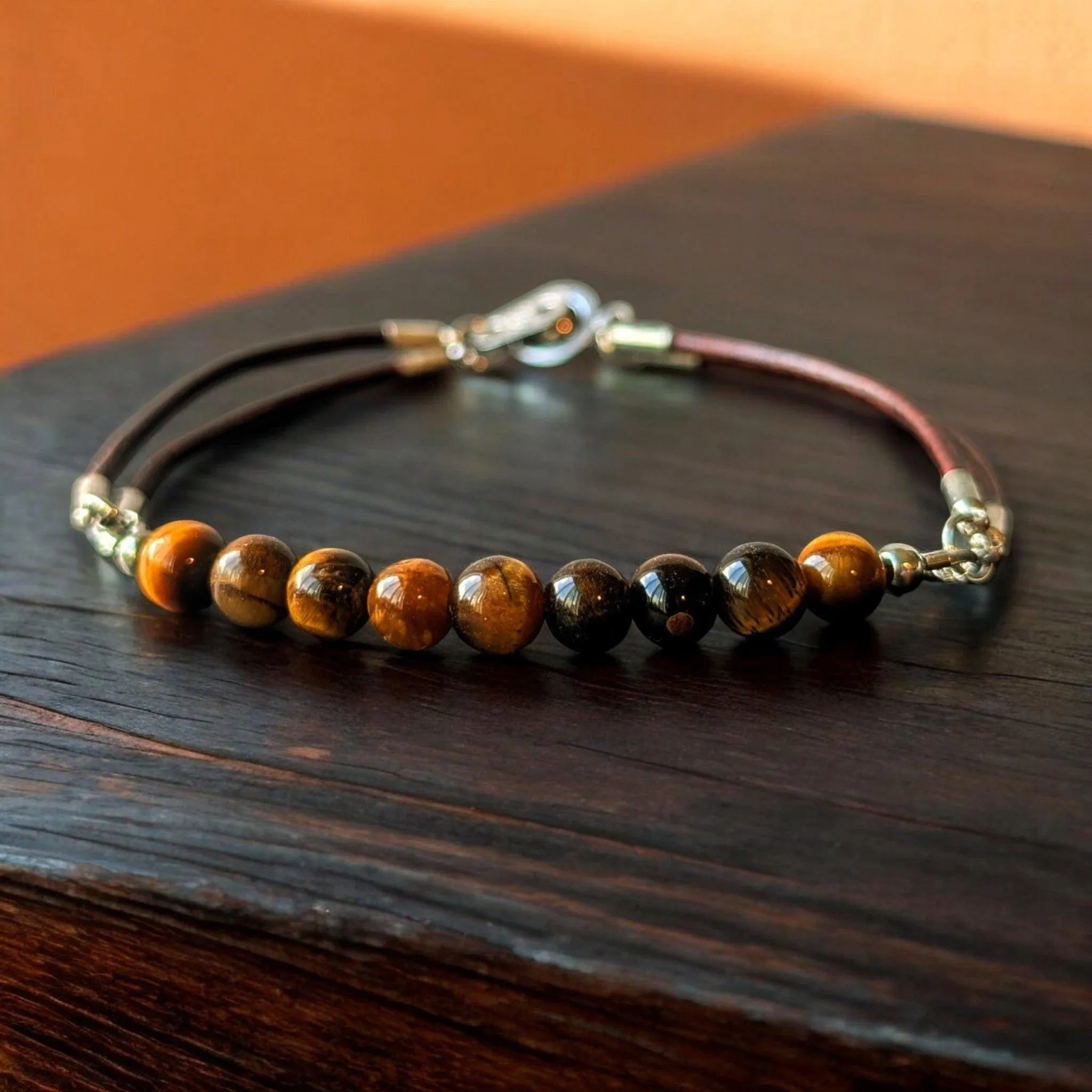 Brown leather bracelet with tiger's eye stone beads and silver-tone clasp on wooden surface.