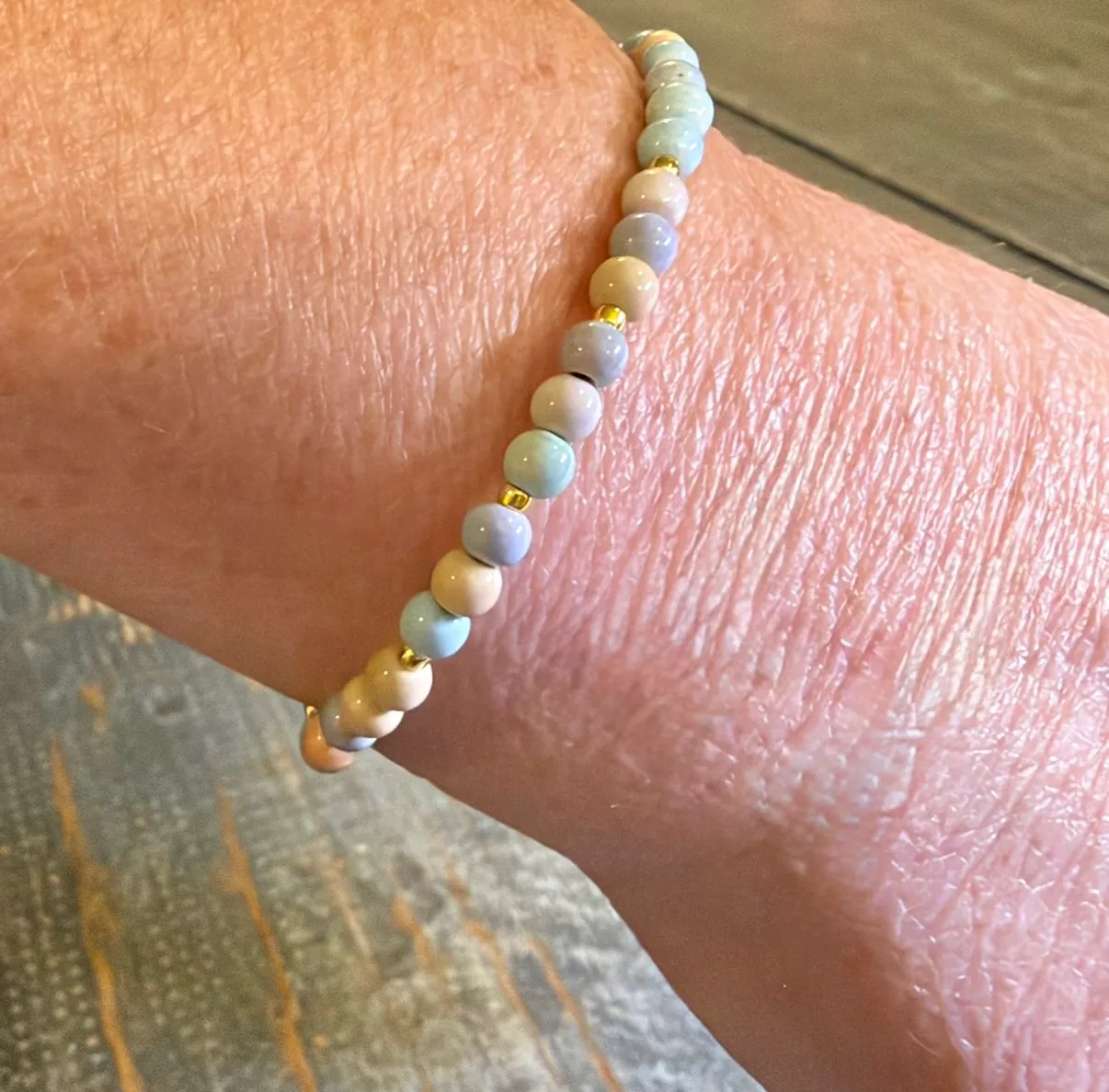 Pastel beaded bracelet with gold spacer beads worn on wrist.