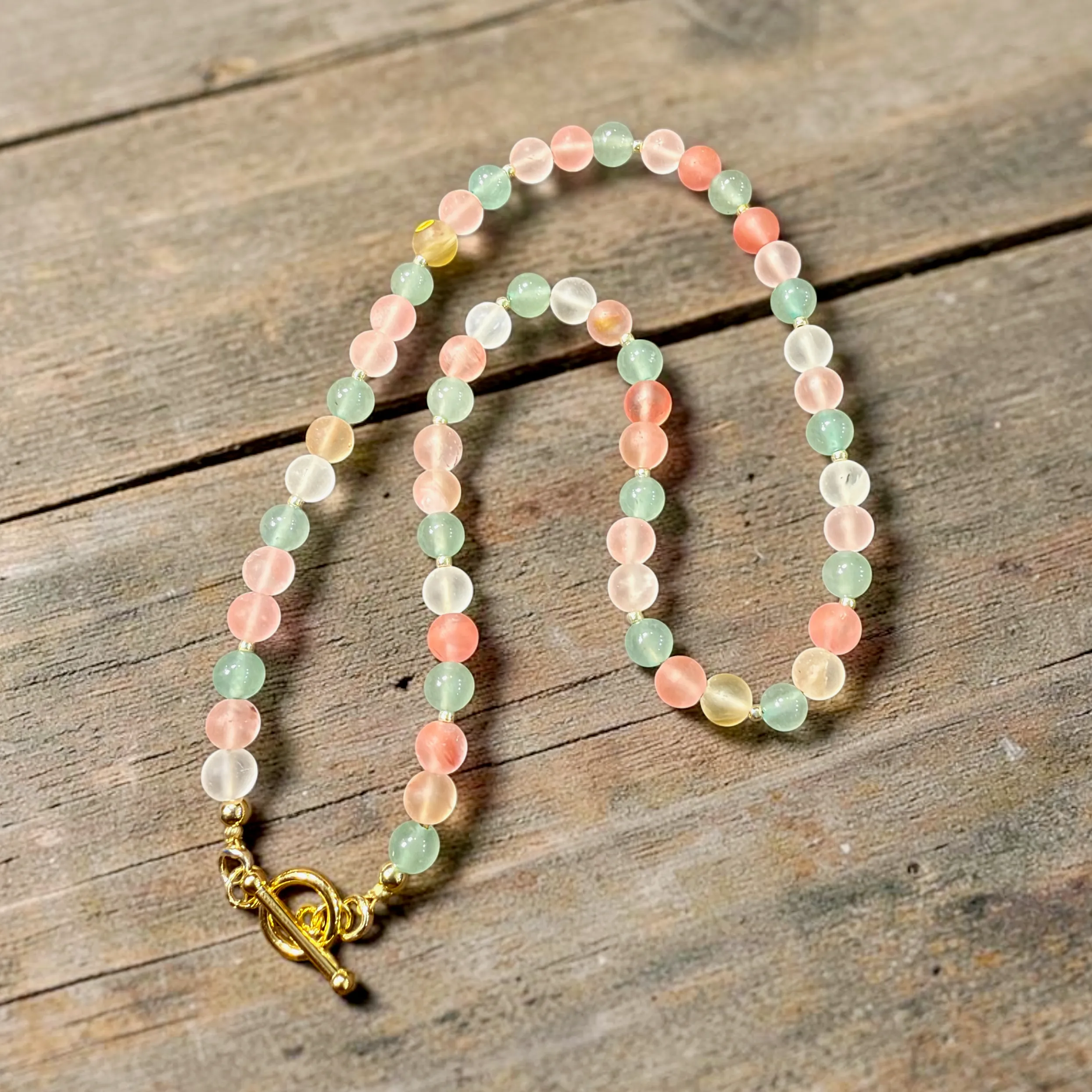 Two beaded bracelets with pink, green, and clear gemstone beads and gold toggle clasps on wooden surface.