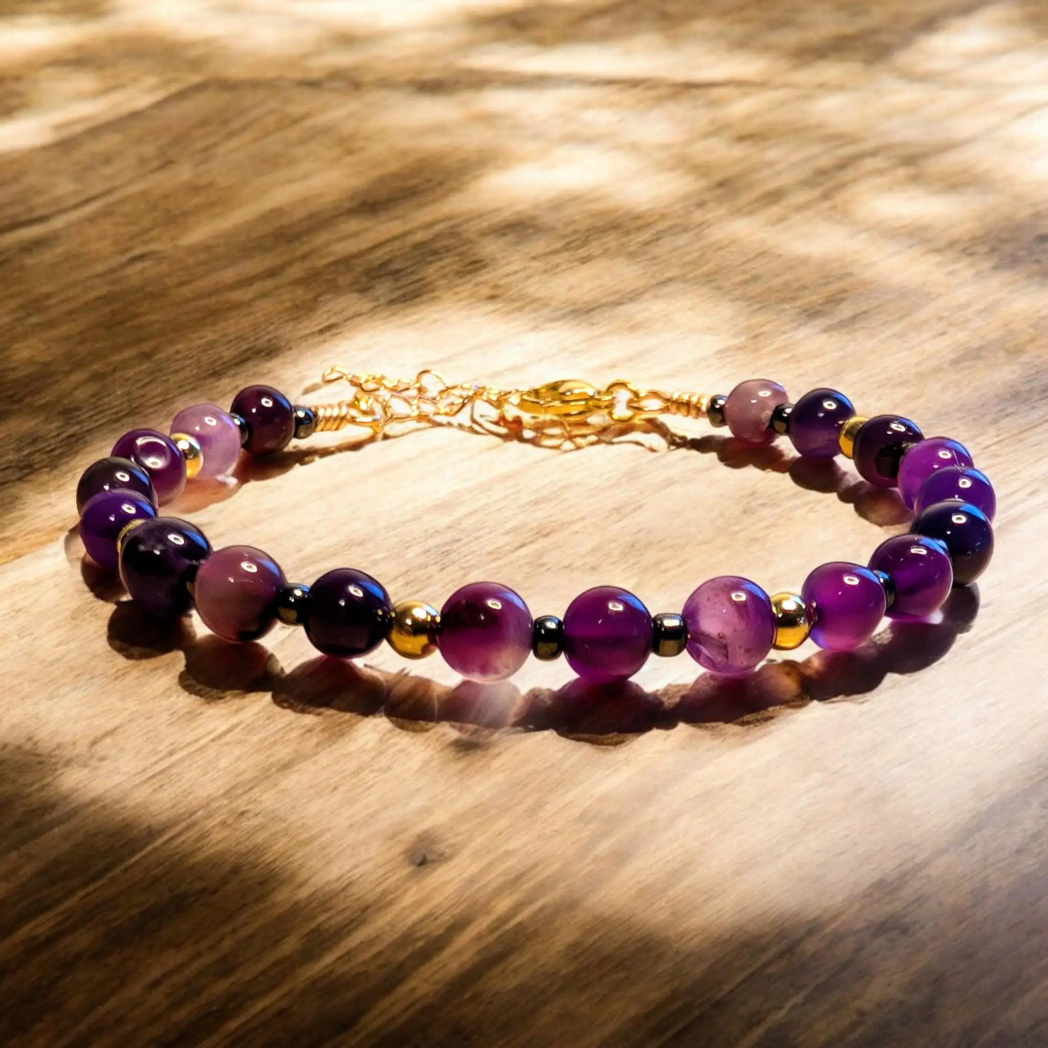 Purple amethyst beaded bracelet with gold-tone chain closure on wooden surface.
