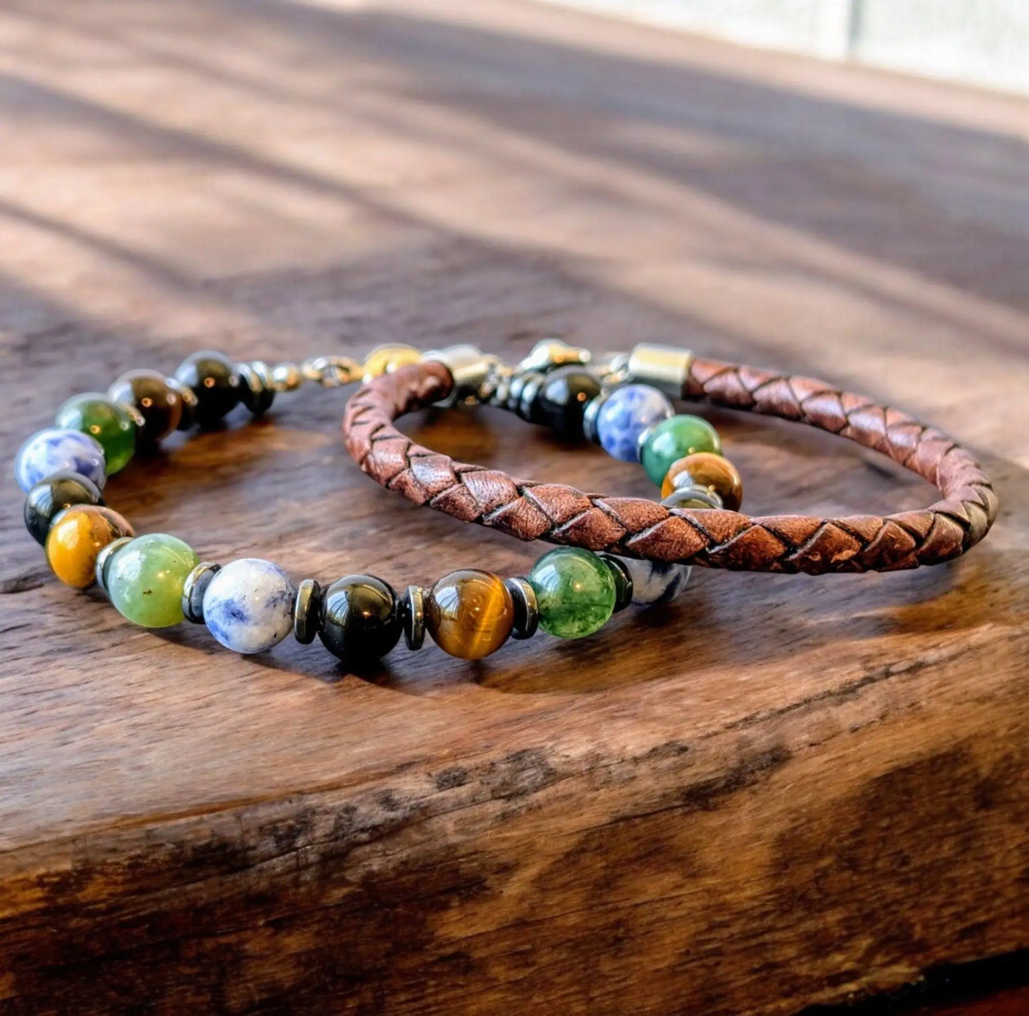 Braided brown leather bracelet with multicolored gemstone beads and metal spacers on wooden surface.