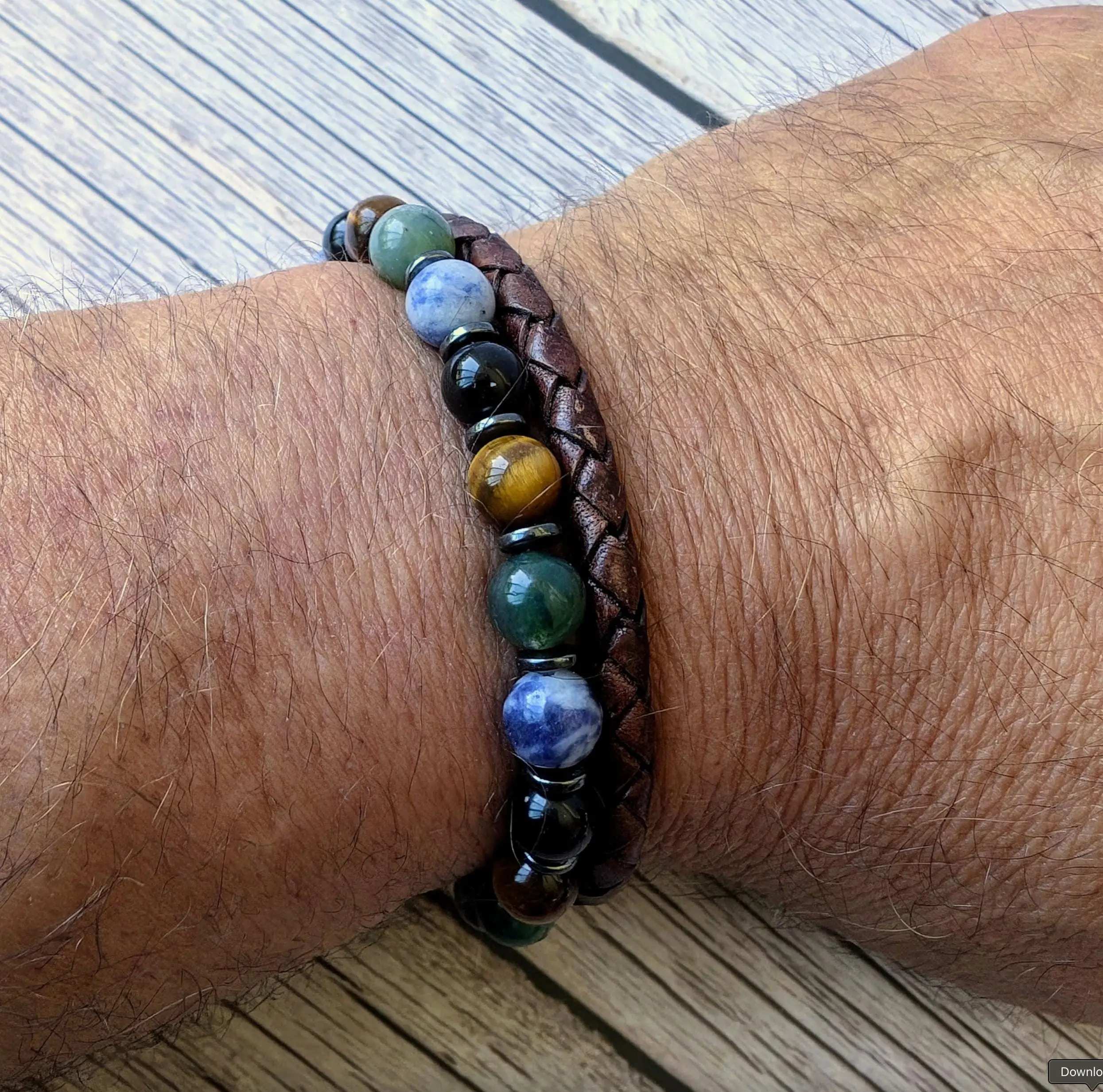 Brown leather beaded bracelet with multicolored gemstone beads including green aventurine, blue sodalite, black onyx, and tiger's eye, worn on wrist.