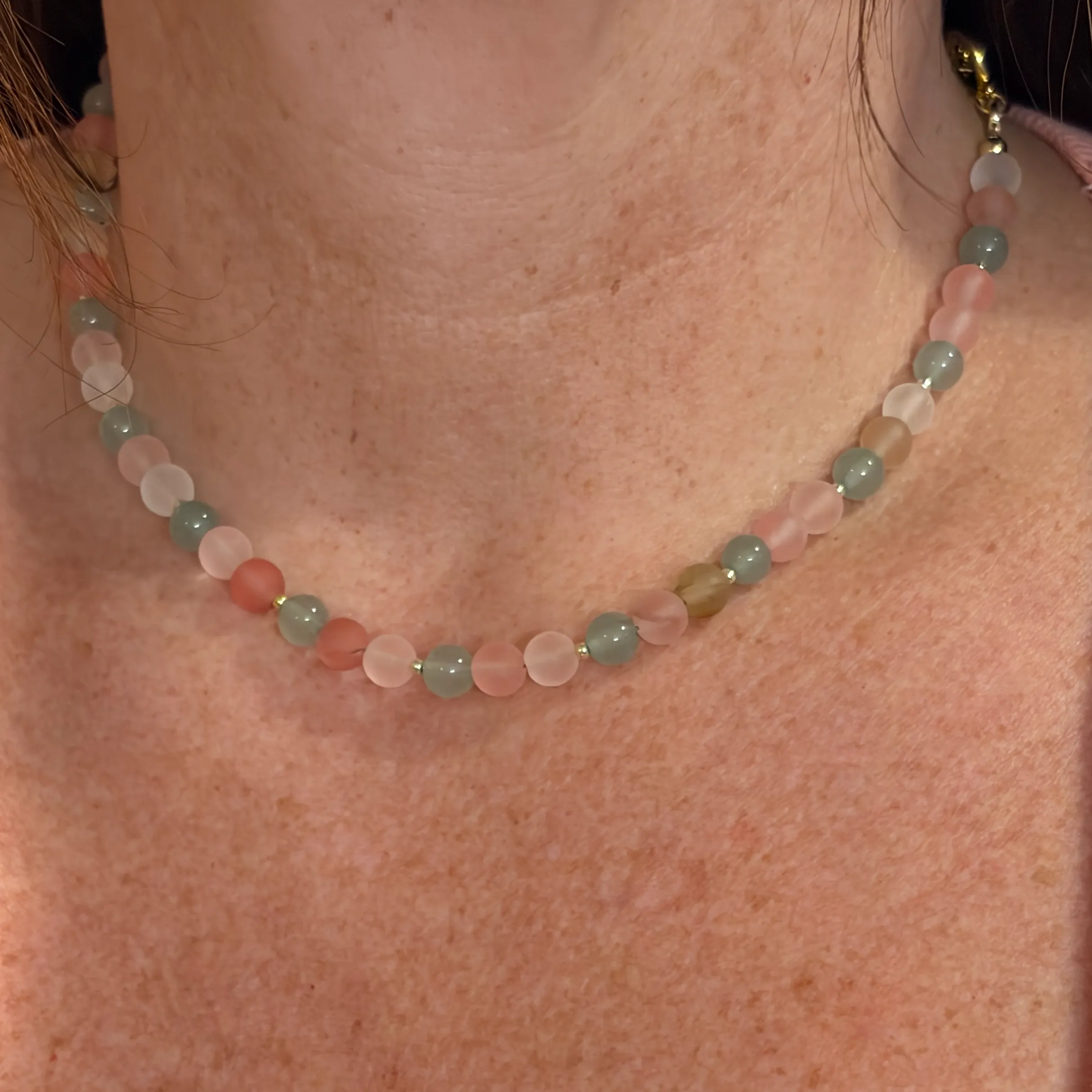 Woman wearing a beaded necklace with alternating rose quartz and green aventurine stones with gold spacers.