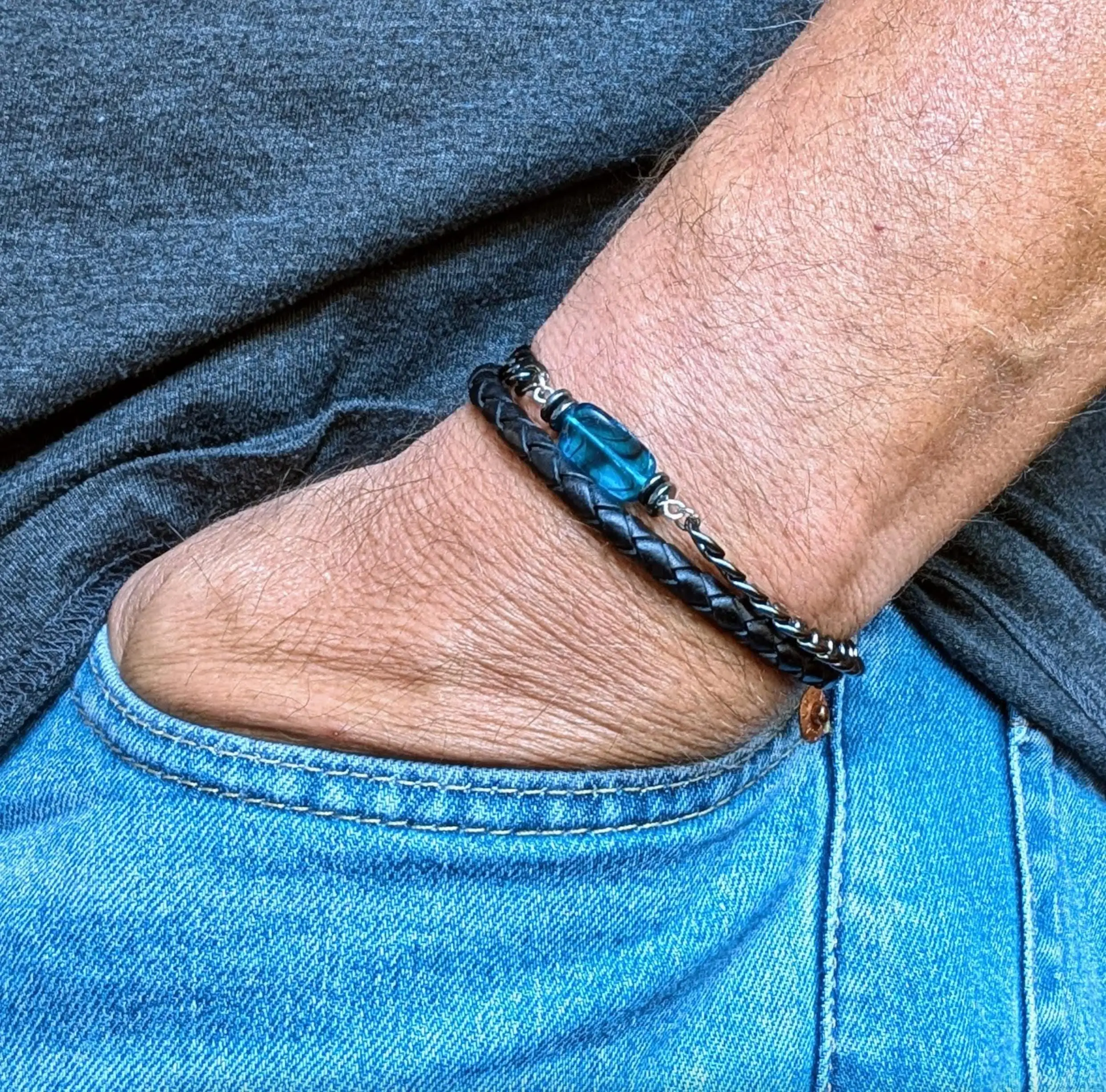 Man wearing a black braided leather bracelet with blue stone centerpiece and silver accents.