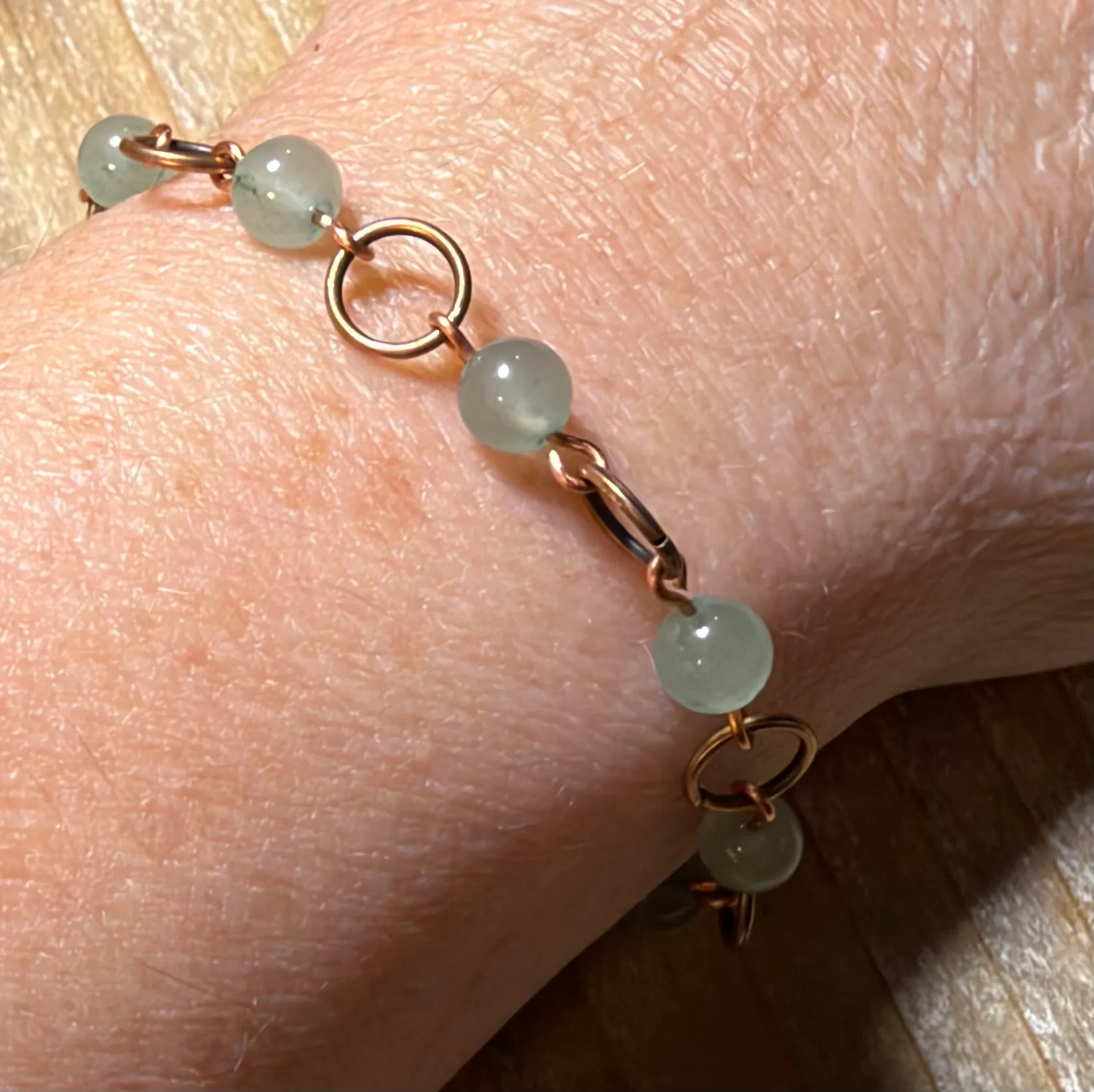 Copper wire bracelet with pale green spherical beads linked by copper loops.