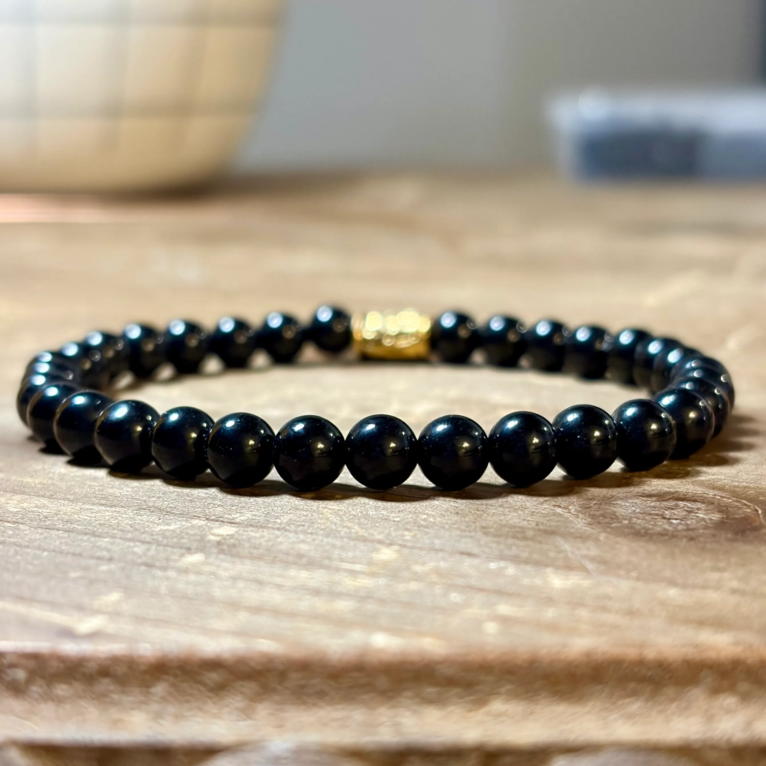 Black onyx beaded bracelet with warm metallic accent bead on wooden surface.