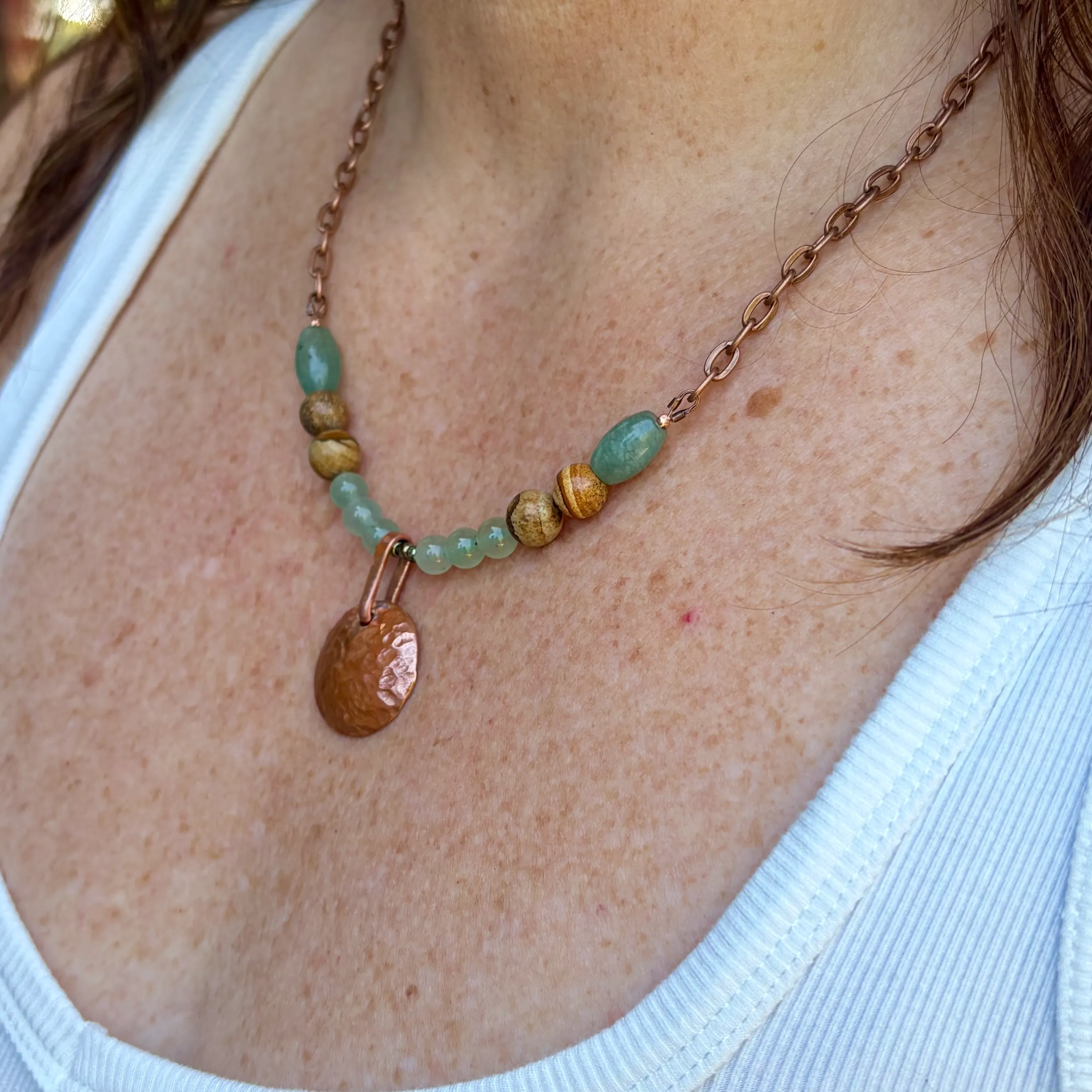 Copper chain necklace with green beads and gold-toned spacers featuring a textured copper pendant.