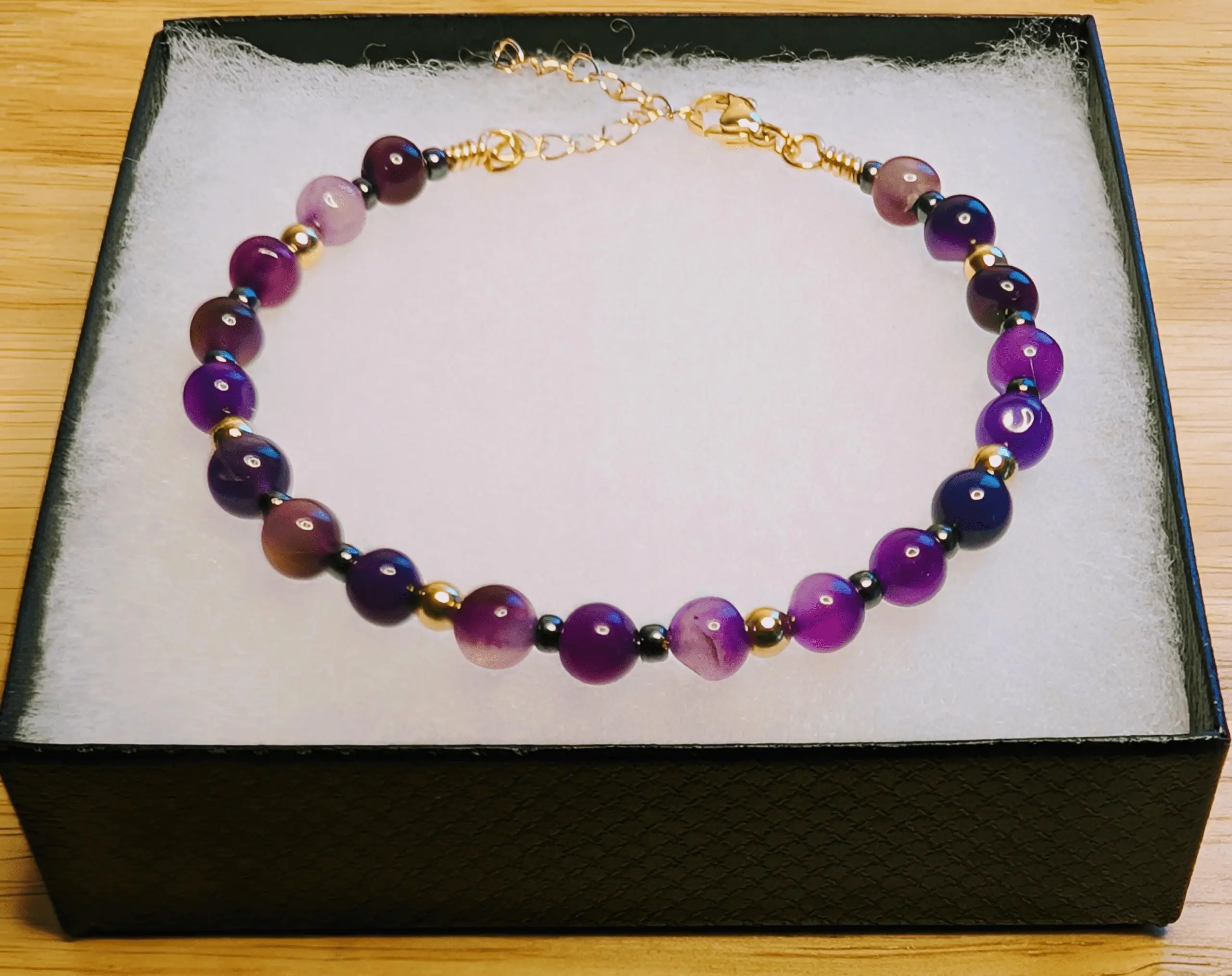 Purple amethyst beaded bracelet with gold and black spacer beads displayed in a black jewelry box.